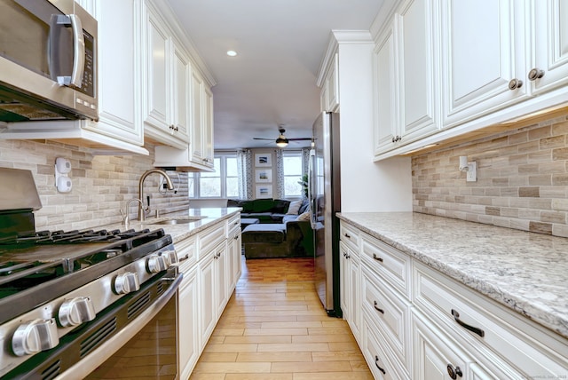 kitchen with sink, ceiling fan, white cabinetry, stainless steel appliances, and light stone counters