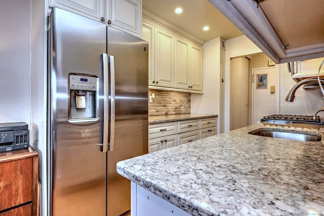 kitchen featuring sink, stainless steel fridge, light stone counters, tasteful backsplash, and cream cabinetry