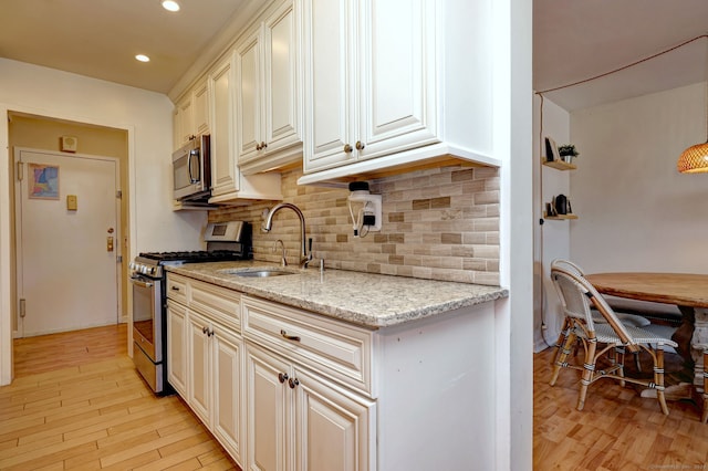 kitchen featuring appliances with stainless steel finishes, sink, decorative backsplash, light stone counters, and light wood-type flooring