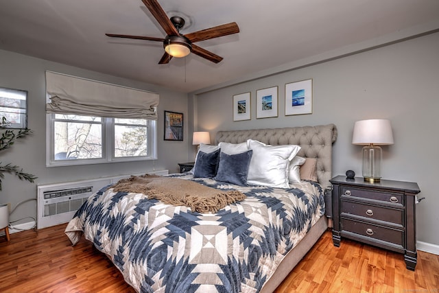 bedroom featuring a wall mounted AC, ceiling fan, and light hardwood / wood-style flooring