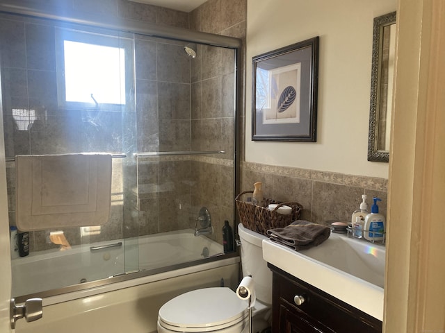 full bathroom with vanity, toilet, combined bath / shower with glass door, and tile walls