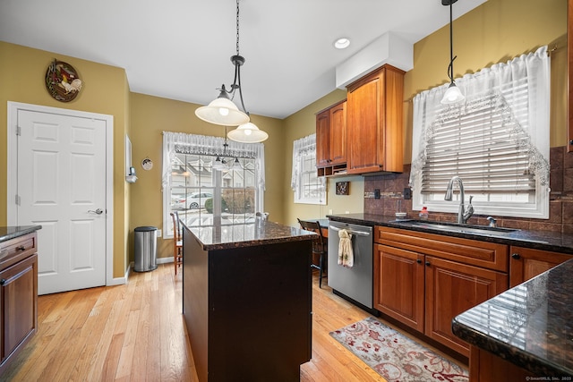 kitchen featuring decorative light fixtures, dishwasher, sink, a center island, and light hardwood / wood-style flooring