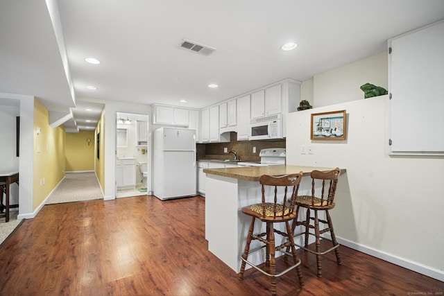 kitchen featuring white cabinetry, a kitchen breakfast bar, decorative backsplash, kitchen peninsula, and white appliances