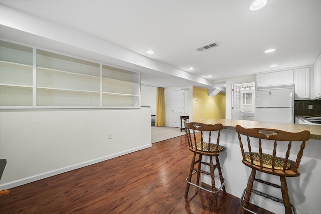 kitchen featuring a kitchen bar, dark hardwood / wood-style flooring, kitchen peninsula, white fridge, and white cabinets