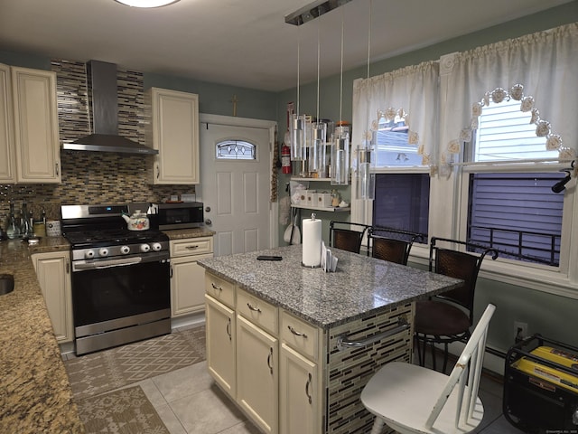 kitchen with pendant lighting, stainless steel appliances, light stone countertops, cream cabinetry, and wall chimney exhaust hood