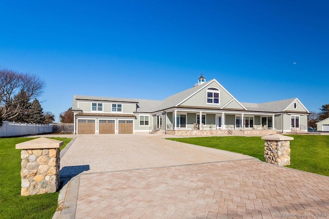 view of front facade with decorative driveway, covered porch, an attached garage, fence, and a front lawn