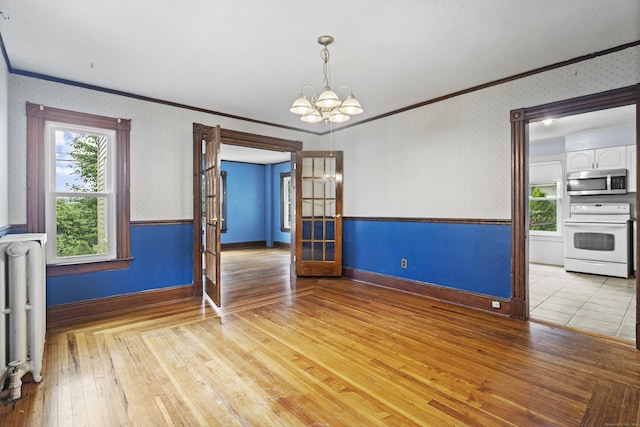 empty room with radiator, crown molding, light hardwood / wood-style floors, french doors, and a chandelier