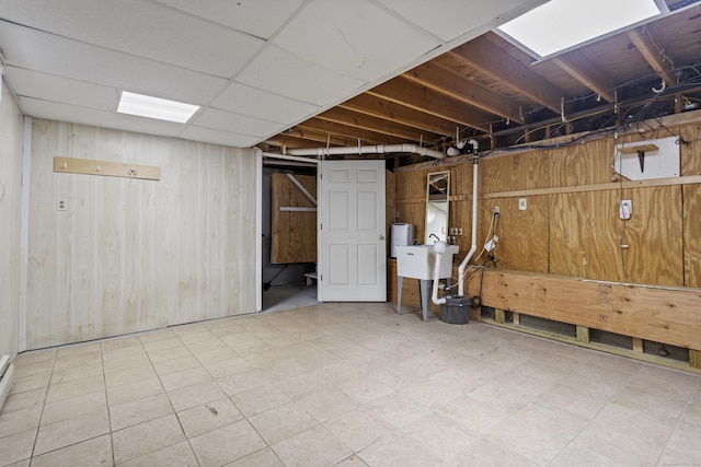 basement featuring a drop ceiling, sink, and wooden walls