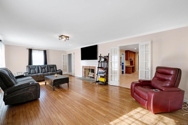 living room with a fireplace, crown molding, light hardwood / wood-style flooring, and french doors