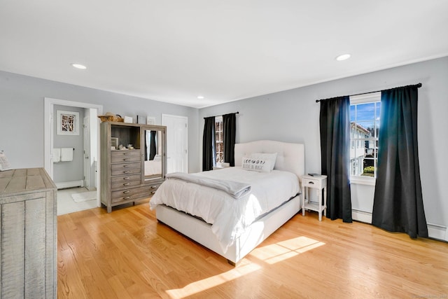 bedroom featuring connected bathroom, a baseboard heating unit, and light wood-type flooring