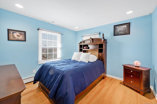 bedroom with light hardwood / wood-style floors and a baseboard heating unit