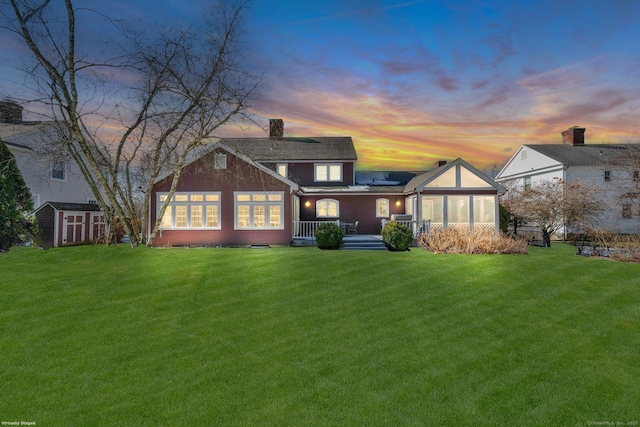 back house at dusk featuring a yard and a storage unit