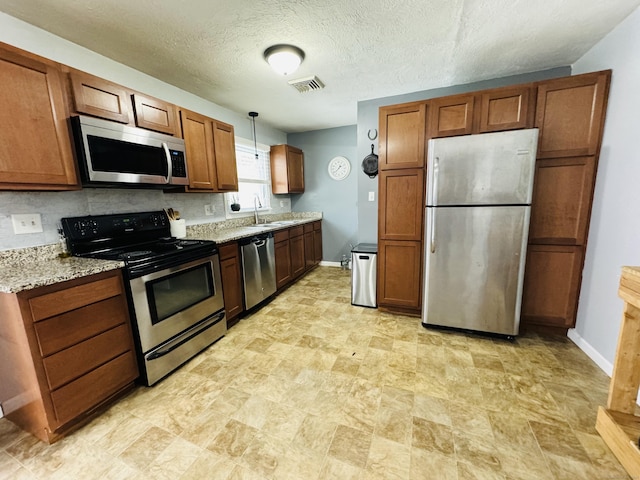 kitchen with appliances with stainless steel finishes, sink, backsplash, hanging light fixtures, and light stone countertops