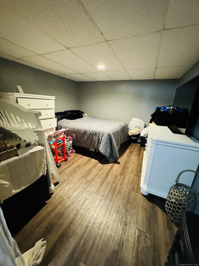 bedroom featuring wood-type flooring, refrigerator, and a drop ceiling