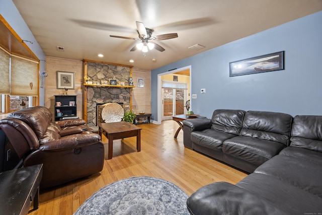 living room with a stone fireplace, light hardwood / wood-style flooring, and ceiling fan