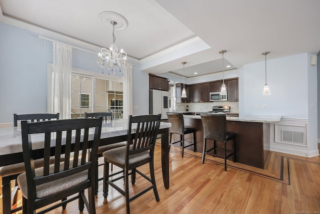 dining room with crown molding, a tray ceiling, a chandelier, and light wood-type flooring