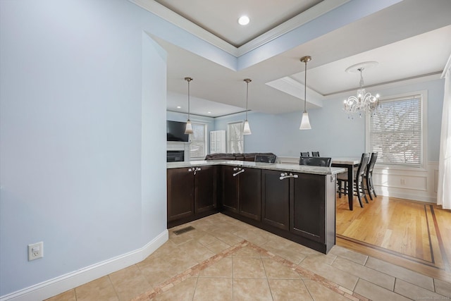 kitchen with light stone counters, ornamental molding, a raised ceiling, light tile patterned flooring, and kitchen peninsula