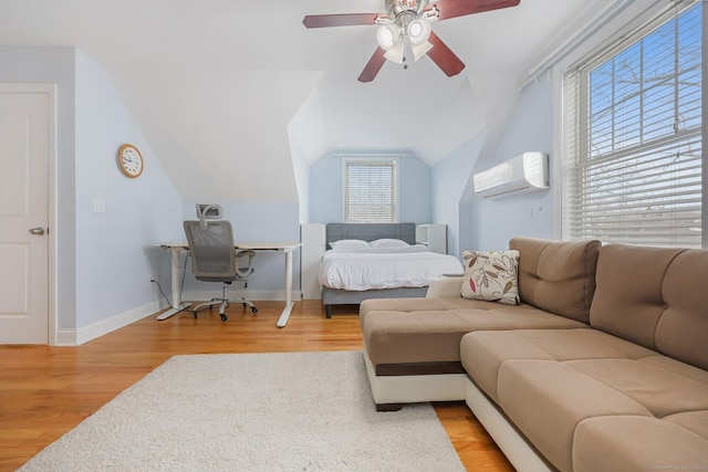 bedroom with vaulted ceiling, a wall mounted AC, ceiling fan, and light hardwood / wood-style flooring