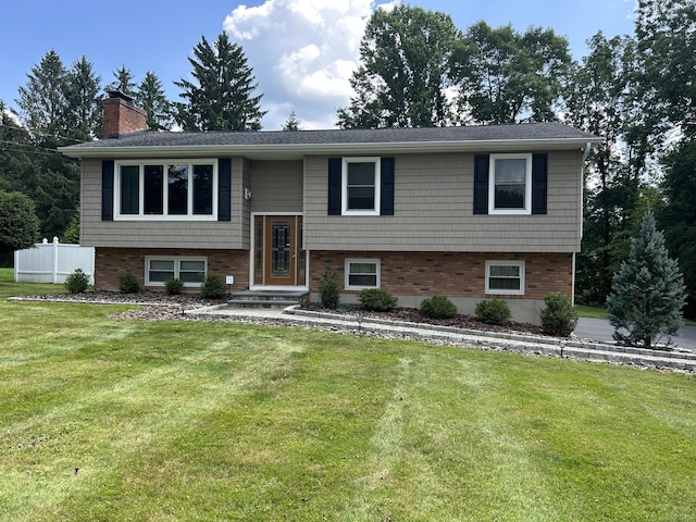 bi-level home with a front yard, brick siding, fence, and a chimney