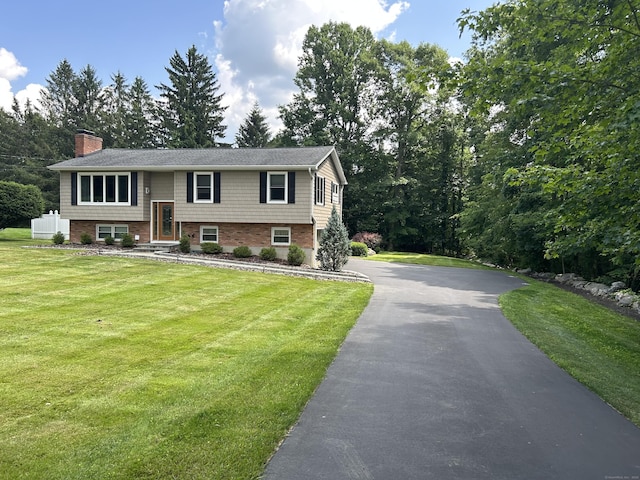 bi-level home featuring driveway, a front lawn, a chimney, and brick siding