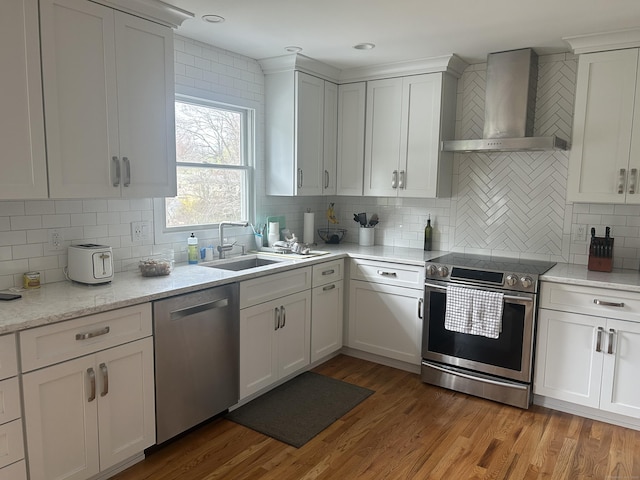 kitchen with a sink, appliances with stainless steel finishes, light wood-type flooring, decorative backsplash, and wall chimney exhaust hood