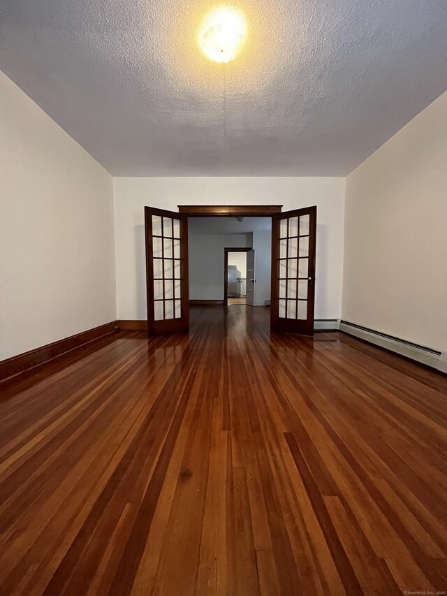 unfurnished room with a baseboard heating unit, dark wood-type flooring, a textured ceiling, and french doors