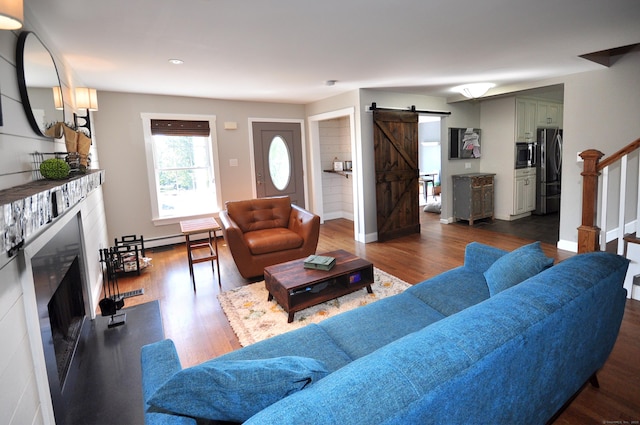 living room with a fireplace, stairway, a barn door, a baseboard heating unit, and wood finished floors