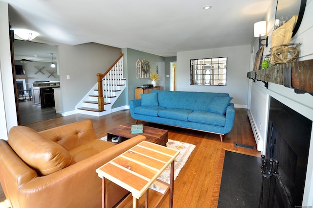 living room with stairs, wood finished floors, a baseboard radiator, and a fireplace with flush hearth