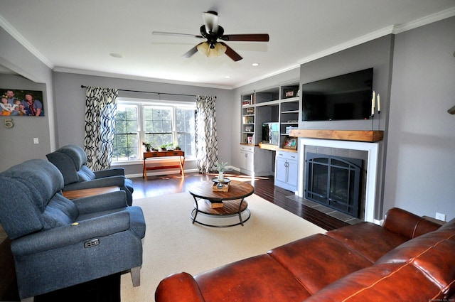 living area with baseboards, dark wood finished floors, a tiled fireplace, ceiling fan, and ornamental molding