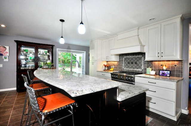 kitchen with light stone counters, premium range hood, a sink, backsplash, and stainless steel range