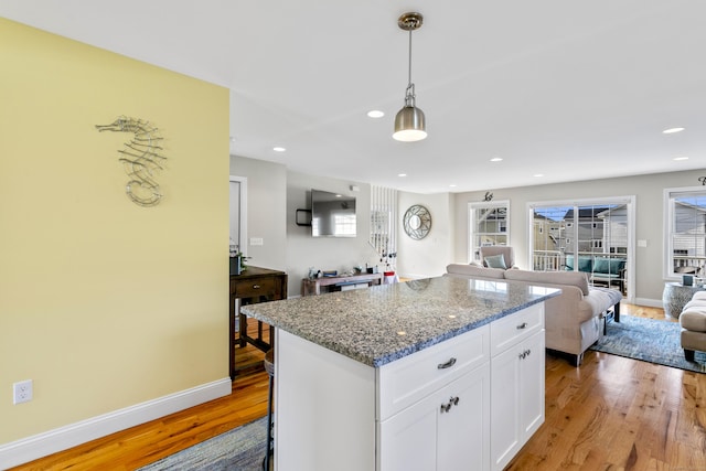 kitchen with a kitchen island, white cabinets, hanging light fixtures, light hardwood / wood-style floors, and light stone countertops