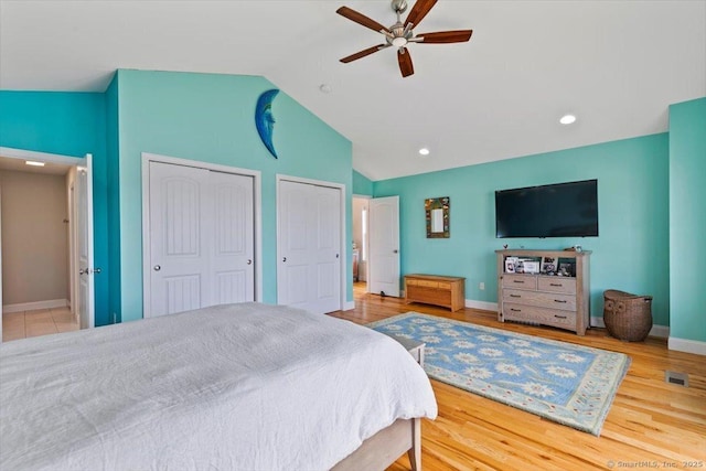 bedroom with ceiling fan, two closets, vaulted ceiling, and wood-type flooring