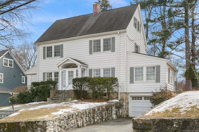 colonial inspired home with a garage, concrete driveway, a shingled roof, and a chimney