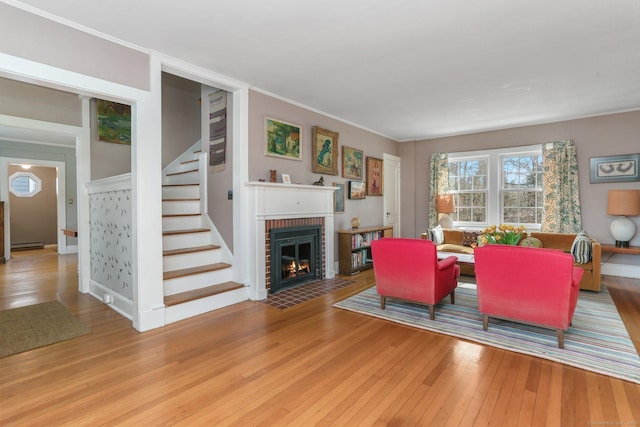 living area with light wood-style flooring, ornamental molding, baseboard heating, stairway, and a brick fireplace