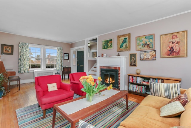 living area featuring ornamental molding, a brick fireplace, baseboards, and light wood finished floors