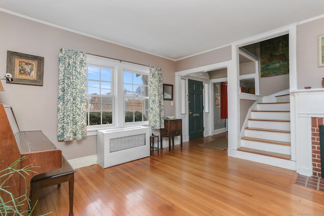 interior space featuring hardwood / wood-style flooring, radiator heating unit, ornamental molding, stairs, and a brick fireplace