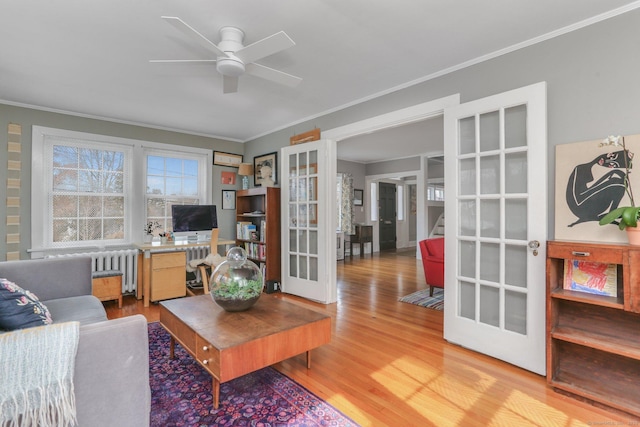 living room with french doors, radiator heating unit, light wood-style floors, ornamental molding, and a ceiling fan