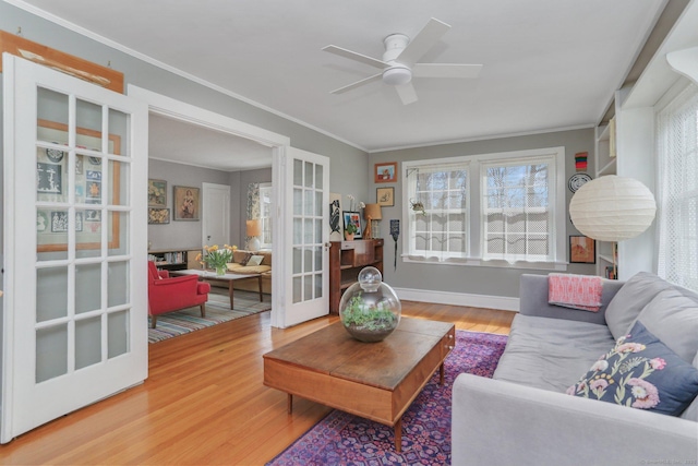 living area with french doors, ornamental molding, ceiling fan, wood finished floors, and baseboards