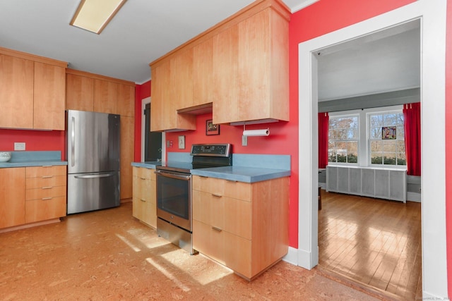 kitchen featuring stainless steel appliances, light brown cabinetry, and radiator