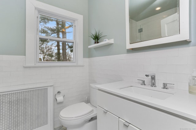 bathroom featuring toilet, a wainscoted wall, tile walls, vanity, and radiator