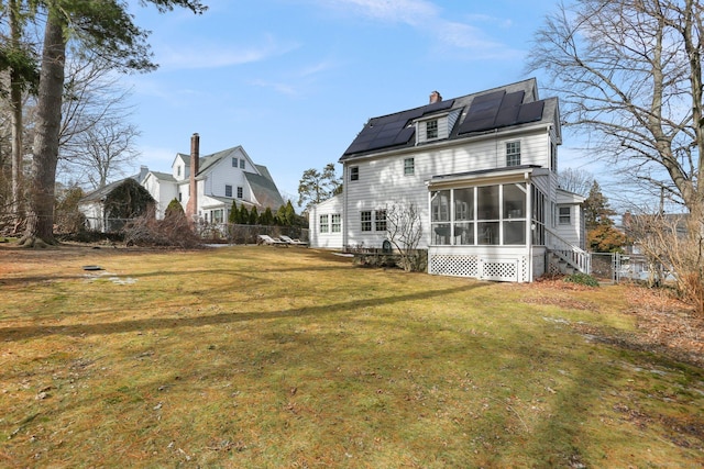 rear view of property with solar panels, a sunroom, a chimney, fence, and a yard