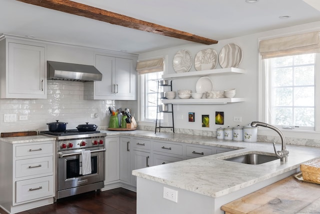 kitchen featuring sink, premium stove, kitchen peninsula, light stone countertops, and wall chimney range hood