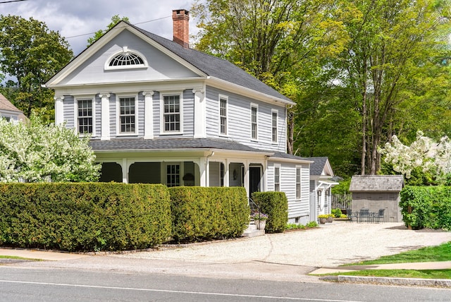 view of front of home featuring a chimney, an outdoor structure, gravel driveway, and covered porch