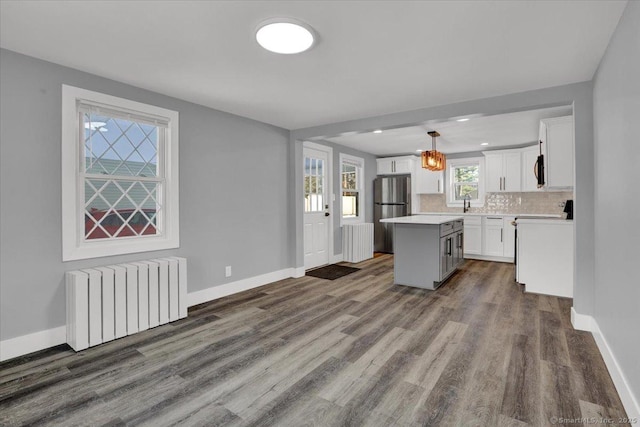 kitchen with pendant lighting, stainless steel fridge, radiator heating unit, white cabinets, and a kitchen island