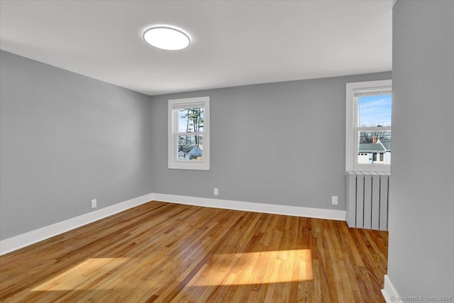 spare room featuring light hardwood / wood-style flooring, radiator heating unit, and a healthy amount of sunlight