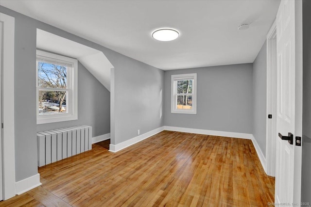 additional living space with lofted ceiling, radiator heating unit, and light wood-type flooring