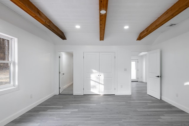 unfurnished bedroom with beam ceiling, light hardwood / wood-style floors, and multiple windows