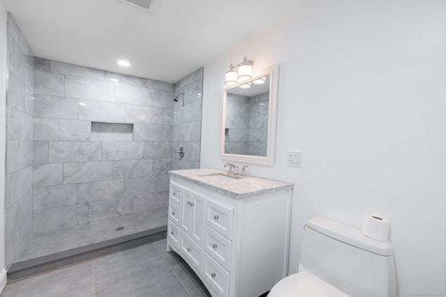 bathroom featuring vanity, a tile shower, tile patterned floors, and toilet