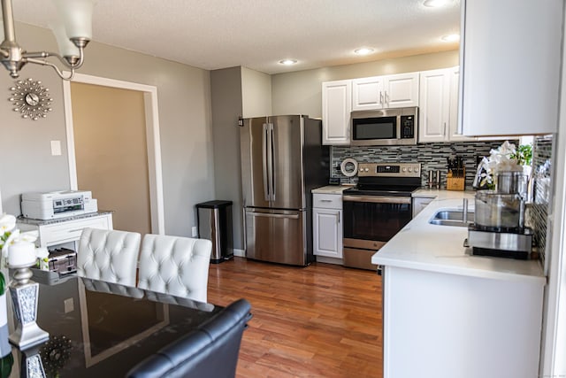 kitchen with appliances with stainless steel finishes, tasteful backsplash, a textured ceiling, white cabinets, and dark hardwood / wood-style flooring