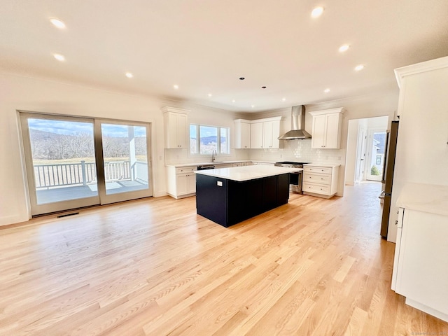 kitchen featuring sink, appliances with stainless steel finishes, white cabinets, a kitchen island, and wall chimney exhaust hood